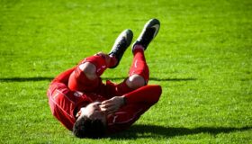 Man rolling on the grass in pain because of leg cramps