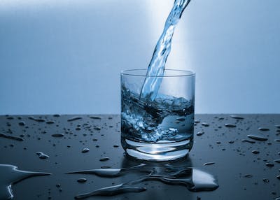 Water is being poured into a glass on a table -Why is Water Important to Your Health