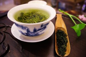 A Teacup of Green Tea and Leaves on a Spatula Beside it - Herbal Remedies for Inflammation