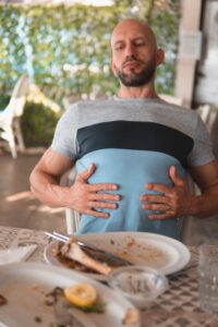A Man With a Distended Abdomen who Has Just Finished Eating a Very Big Plate of Food 