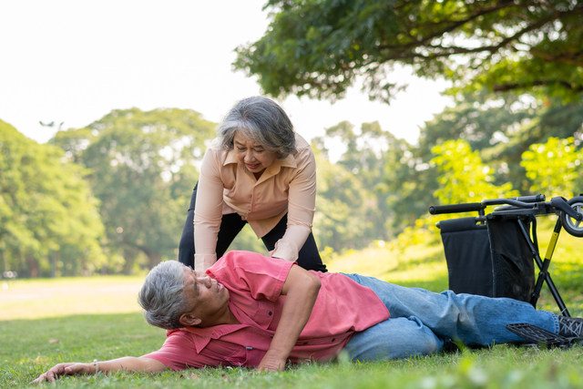 A fallen Asian senior man from his wheelchair lying on the grass bad being assisted by a woman - Safety in the Bedroom
