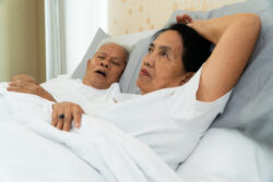 Elderly insomnia in a woman wide awake beside her sleeping husband - Foods that Promote better Sleep