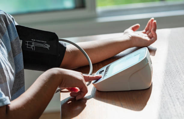 Woman measuring her blood pressure at home while sitting at a table with the blood pressure cuff on her arm and with the other hand, she is pressing the start button on the device - 5 Best and Most Accurate Blood Pressure Monitoring Devices