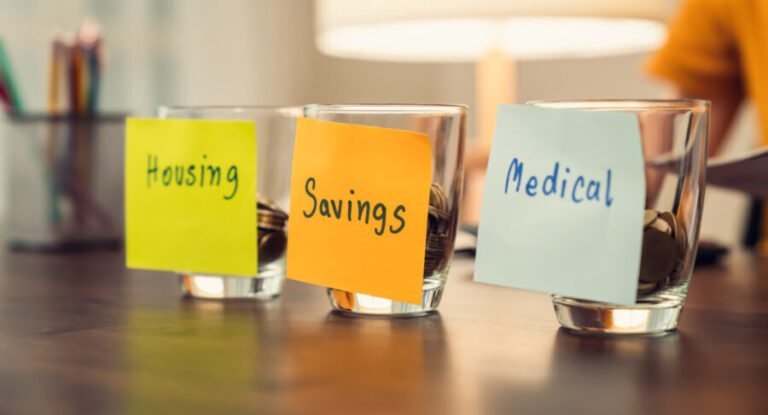 Budget concept Sticky notes on 3 glasses on a table holding some coins medical savings housing e1761374854308
